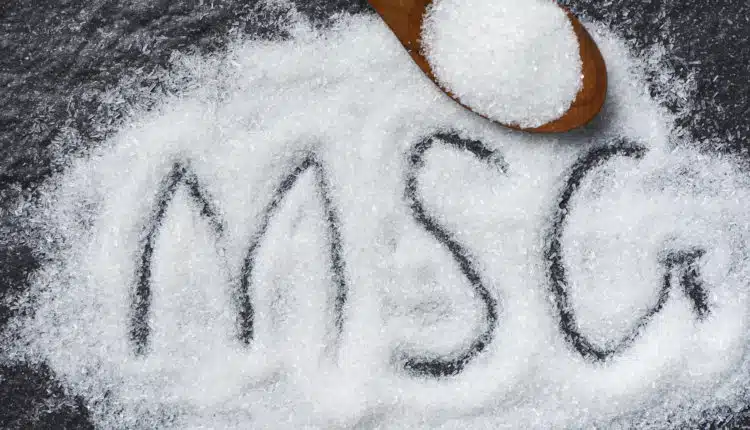 Heap of monosodium glutamate on wooden spoon and dark background – text MSG